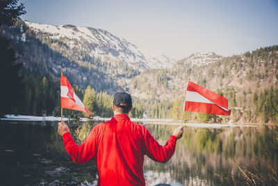 Rear view of man holding flags while standing by lake