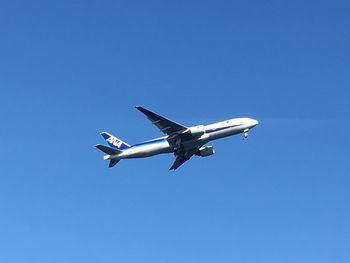 Low angle view of airplane flying against clear blue sky