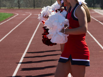 A row of high school cheerleaders holding their pom poms in front on the sidelines of a game.