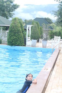 Portrait of woman standing by swimming pool against sky