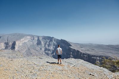 Rear view of man standing on mountain against sky