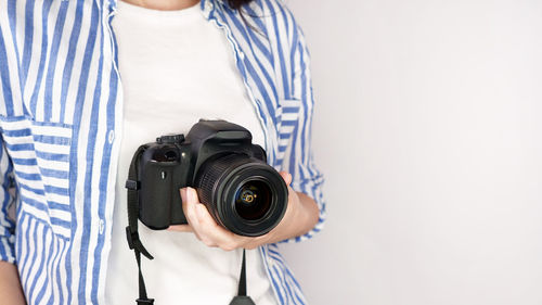 Midsection of woman photographing with camera against wall