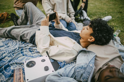 Teenage boy using smart phone while lying on male friend in public park