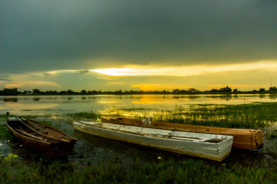 Boats moored on lake against sky during sunset