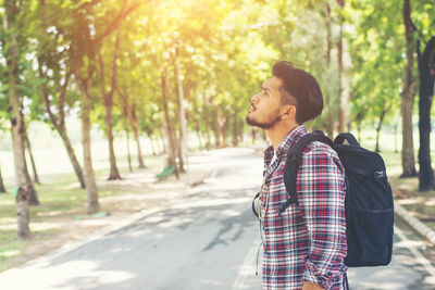 Side view of young man with backpack looking away while standing on road
