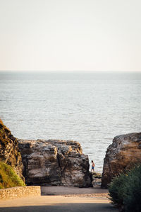 Scenic view of sea with shirtless man seen through rocks against clear sky