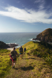 Rear view of people walking on shore by sea against sky