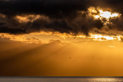 Scenic view of sea against dramatic sky during sunset