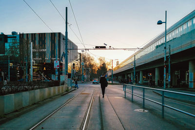 Rear view of man walking on street in city against sky