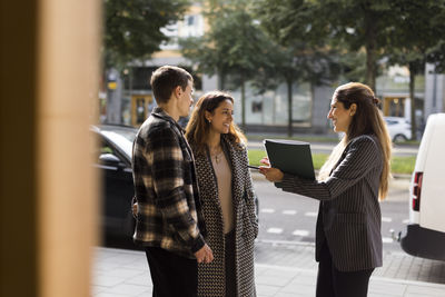 Smiling saleswoman talking with couple while standing at street