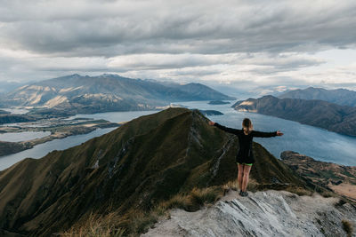 Rear view of woman standing on top of mountain with outstretched arms