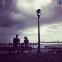 Man sitting on bench against cloudy sky