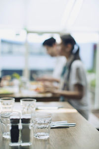 Drinking glasses with salt and pepper shaker on table with couple in background