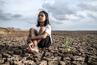 Sad girl sitting on cracked land