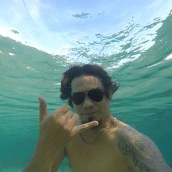 Portrait of shirtless man gesturing while swimming in sea