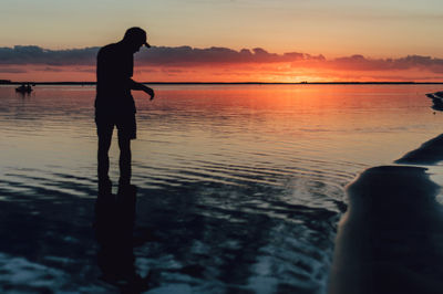 Silhouette man standing on beach against sky during sunset