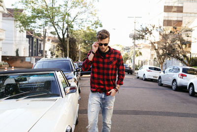 Man wearing plaid shirt and sunglasses while walking on road