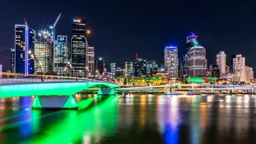 Illuminated bridge over river against buildings in city at night