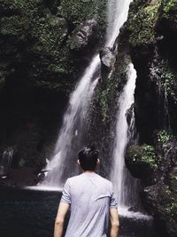 Rear view of man looking at waterfall in forest