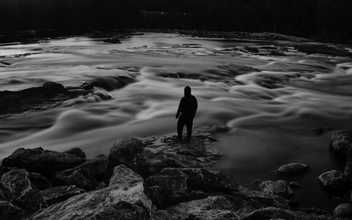 Rear view of man standing on rock in sea