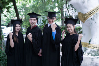 Portrait of happy students in university gowns standing outdoors