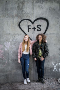 Full length portrait of smiling friends standing against graffiti on gray wall