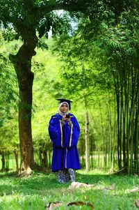 Portrait of woman wearing graduation gown while standing in forest