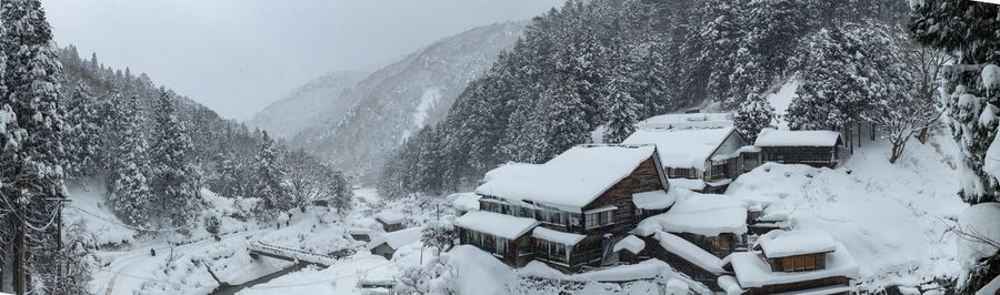 Snow covered trees and buildings against mountain