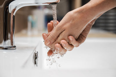 Close-up of woman hand with faucet in water at home