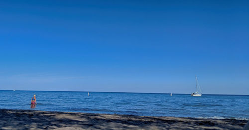 Sailboat sailing in sea against clear blue sky