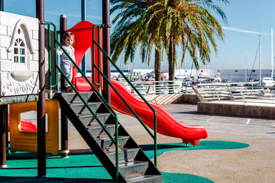 Girl looking away while playing on red slide at playground