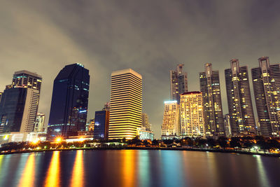 Illuminated city by river against sky at night