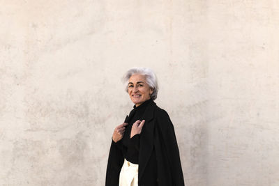 Portrait of smiling woman standing against wall