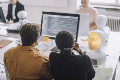 Rear view of multiracial male and female students discussing over computer in innovation lab