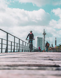 Man riding bicycle on bridge in city against sky