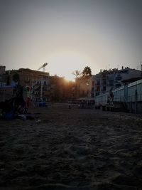 People in city against clear sky during sunset