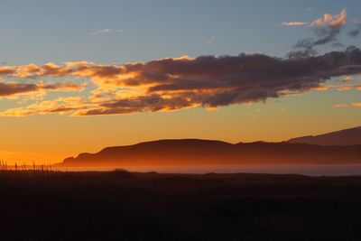 Scenic view of dramatic sky over silhouette landscape during sunset
