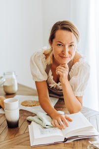 Woman with recipe book looking at camera while cooking at kitchen and