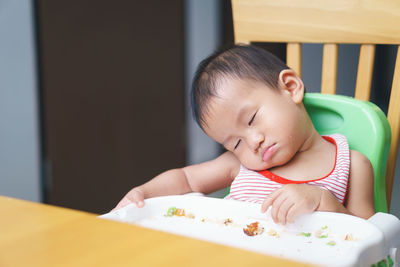 Cute boy sleeping on high chair at home