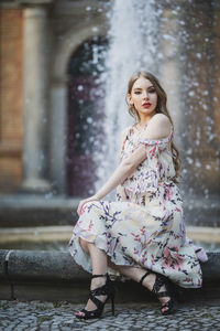 Portrait of beautiful young woman sitting against fountain in city