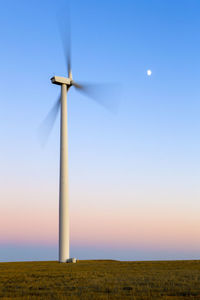 Wind turbine in motion against blue sky with moon