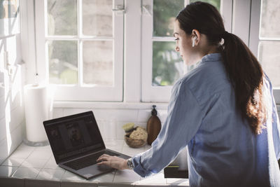 Rear view of female professional using laptop on counter at home office