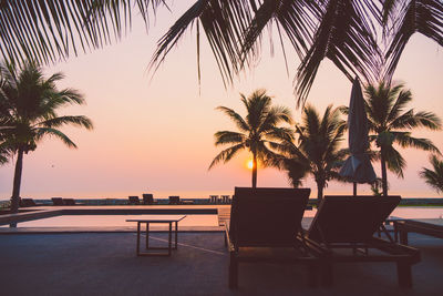 Lounge chair by swimming pool at tourist resort against sky during sunset