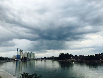 Scenic view of river against cloudy sky in city