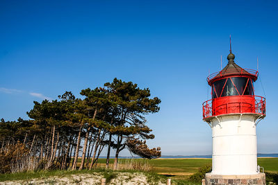 Lighthouse by trees against blue sky