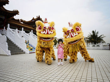 Girl with people in lion costume on footpath against sky