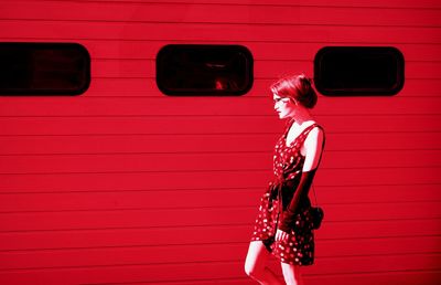 Side view of woman standing against red wall