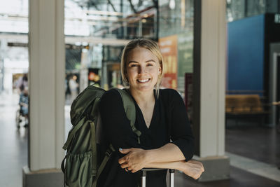 Portrait of smiling woman leaning on luggage at station