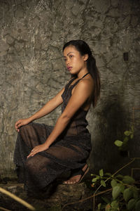 Side view of young woman looking away while crouching against wall