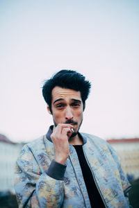 Portrait of young man smoking cigarette against sky